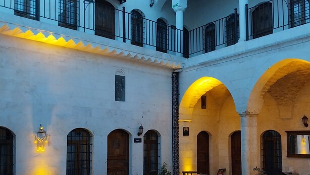 Un patio con mobiliario exterior, suelo de piedra y arcos.