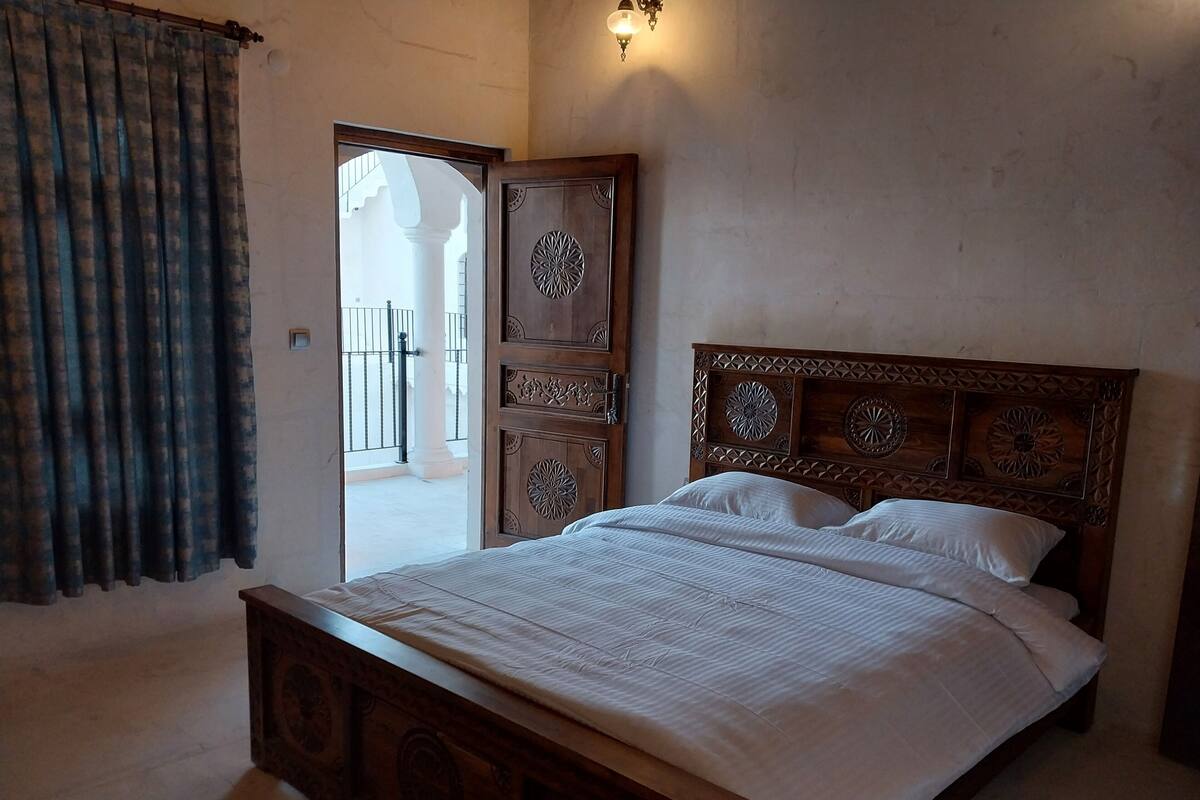 A bedroom with a wooden bed, a door leading to a balcony, and a wall-mounted light fixture.