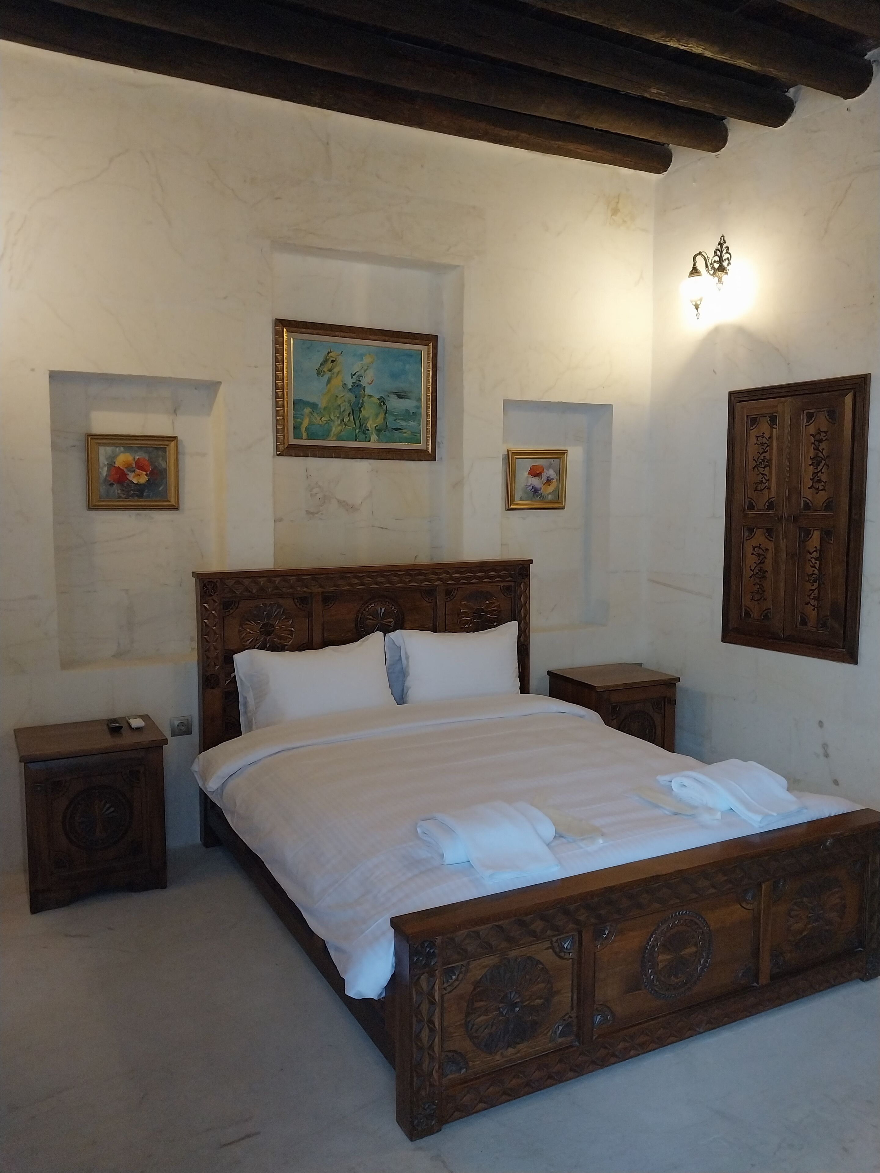 A wooden bed with a headboard, two nightstands, and a wall-mounted light fixture.