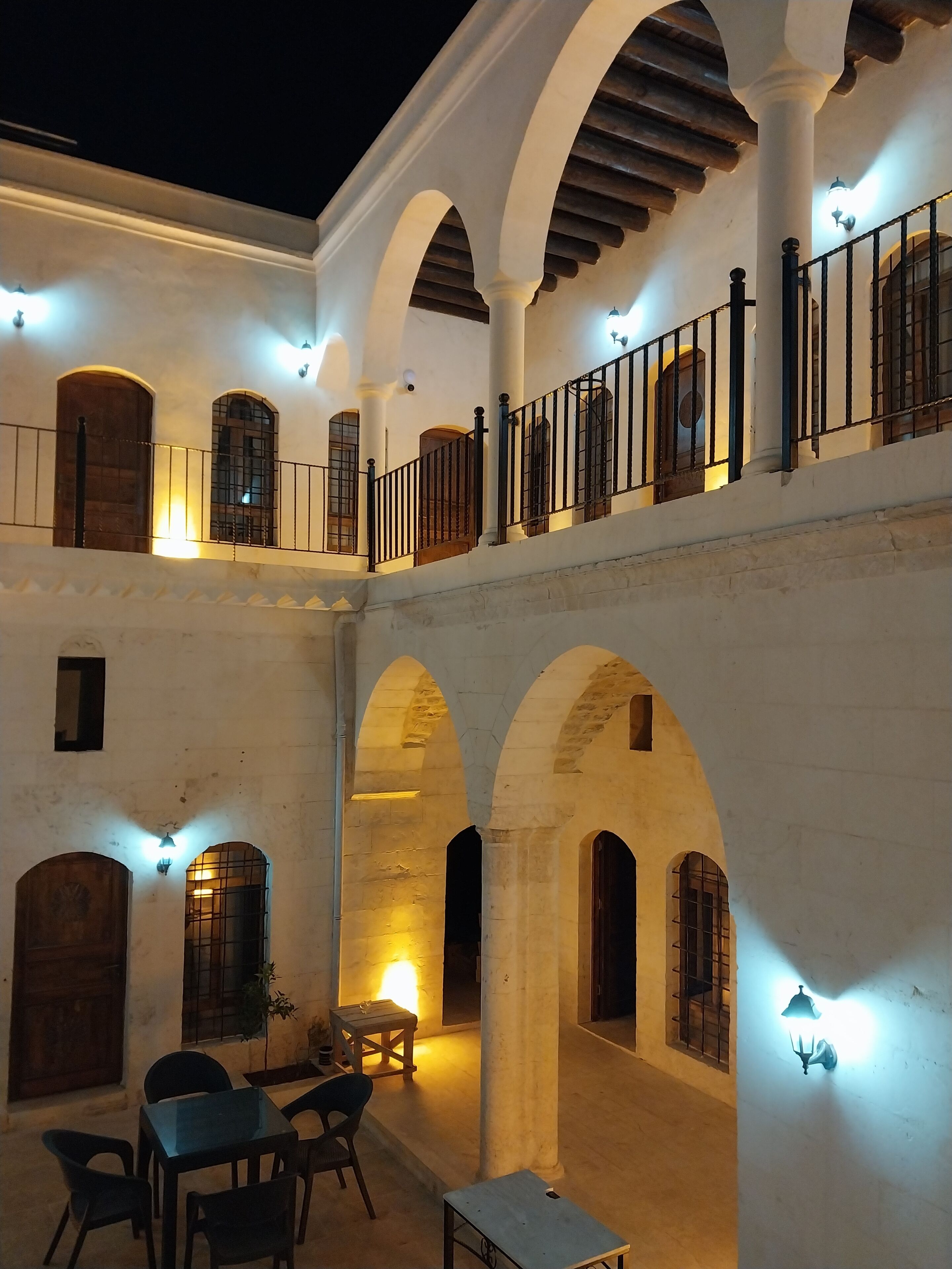 Ein Innenhof mit Bögen, einem Balkon und einer Sitzecke mit Stühlen und Tisch.