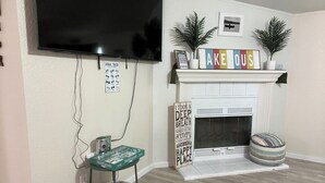 Un salon avec une cheminée, un téléviseur fixé au mur, une petite table sur laquelle se trouve un pot vert, et une pancarte sur laquelle on peut lire : « J’ai pris une grande inspiration, j’ai savouré le paysage, et je me suis dit : voilà mon endroit préféré. »