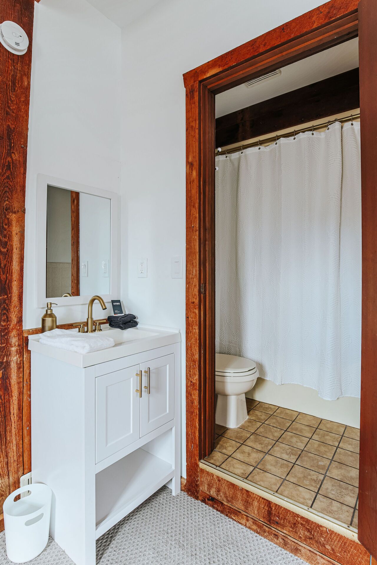 A bathroom with a white vanity, a gold faucet, a mirror, and a shower curtain.