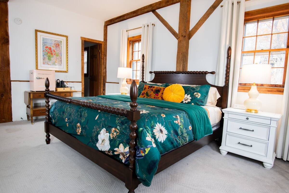 A bedroom with a four-poster bed, a nightstand, a dresser, and a window with curtains.