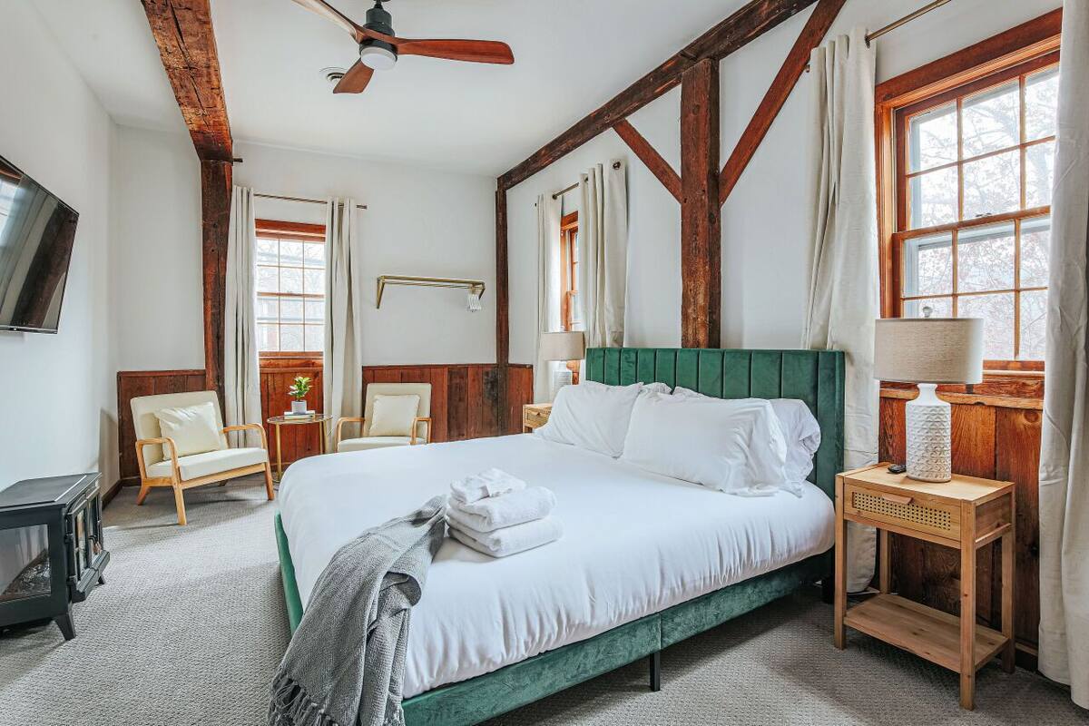 A bedroom with a bed, a wooden headboard, a nightstand, a lamp, a chair, a window, and a ceiling fan.