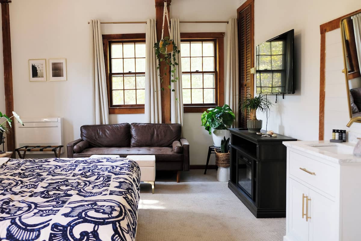 A hotel room with a large bed, a sofa, a desk with a television, and a fireplace.