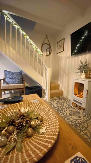 A staircase with a railing, a patterned floor, a table with a decorative centerpiece, a chair, and a fireplace with a mantel. - Award Winning "Smugglers Hide" 2 Bed Harbour House (St Ives, Saint Ives)