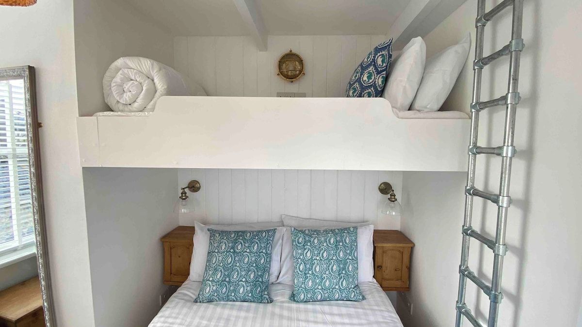 A bunk bed with a ladder, a bedside table, and a wall clock.
