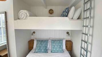 A bunk bed with a ladder, a bedside table, and a wall clock.