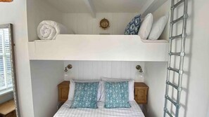 Un lit superposé avec une échelle, une table de chevet et une horloge murale.