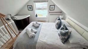 A bedroom with a bed, a window with a view, a radiator, and a wooden ladder.