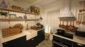 A kitchen with a white sink, black cabinets, a stove, and a hanging pot rack. - Award Winning "Smugglers Hide" 2 Bed Harbour House (St Ives, Saint Ives)