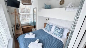 A bedroom with a bunk bed, a wooden bench, a hanging light fixture, and a television mounted on the wall. - Award Winning "Smugglers Hide" 2 Bed Harbour House (St Ives, Saint Ives)