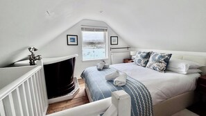 A bedroom with a bed, a window, a radiator, and a small table with a lamp.