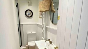 A narrow hallway with a wooden floor, a white sink with a gold faucet, a white toilet, and a white door. - Award Winning "Smugglers Hide" 2 Bed Harbour House (St Ives, Saint Ives)