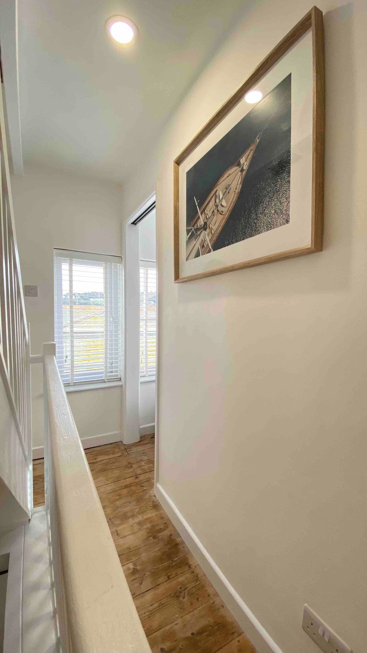 Een gang met een houten vloer, een witte leuning en een ingelijst kunstwerk aan de muur.