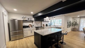 A modern kitchen with a large island, stainless steel appliances, and a black bar seating area. - Spacious 6-bedroom house in marvelous Lubbock with AC, WiFi, fitness room (Lubbock)