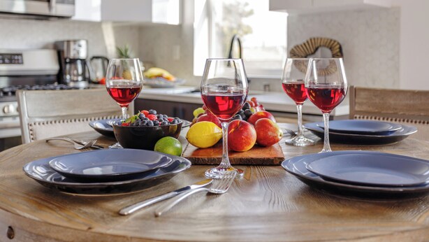 A dining table set with plates, cutlery, and glasses of red wine, accompanied by a bowl of fruit and a wooden board with more fruit. - Stunning Hollywood Townhouse with Sunny views (Los Angeles)