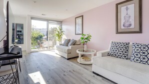 A modern living room with a sofa, a coffee table, and a TV. There is a large window with a view of the outside. - Stunning Hollywood Townhouse with Sunny views (Los Angeles)