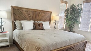 A bed with a wooden headboard, white and brown pillows, a beige blanket, and a bedside table with a lamp.