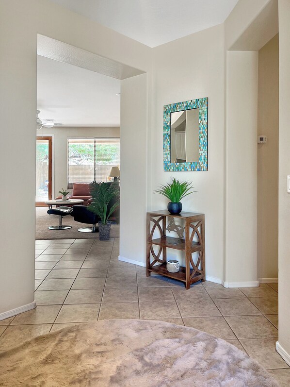Un hall d’entrée spacieux, doté d’un sol carrelé, d’une console en bois ornée d’une plante et d’un miroir décoratif accroché au mur.