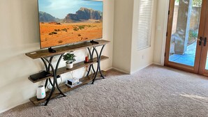 A living room with a mounted TV on a wooden stand, a potted plant, and a door leading outside.