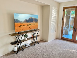 Una sala de estar con una televisión montada sobre un mueble de madera, una planta en maceta y una puerta que da al exterior.