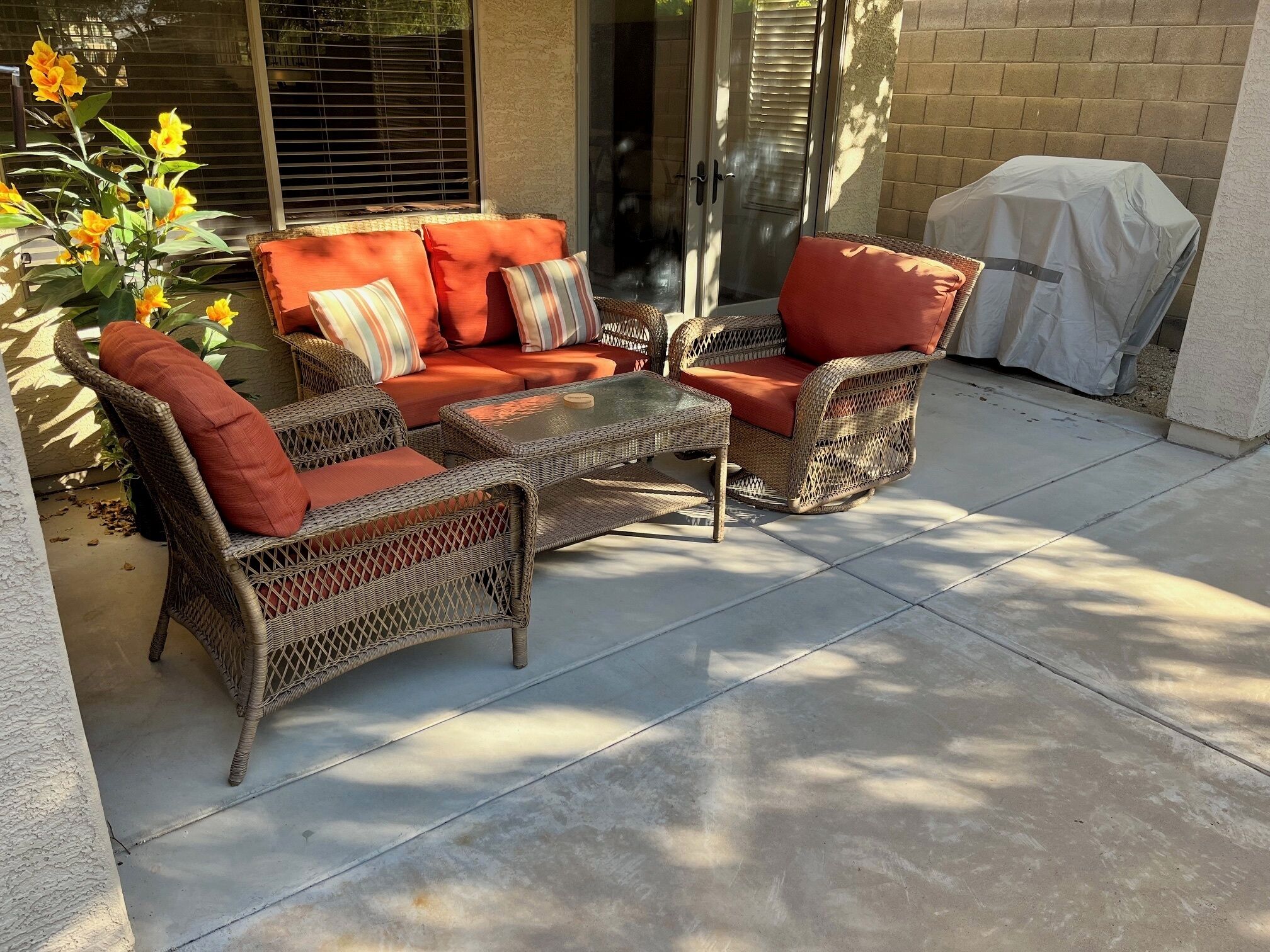 An outdoor patio with wicker furniture, a glass table, and a covered grill.