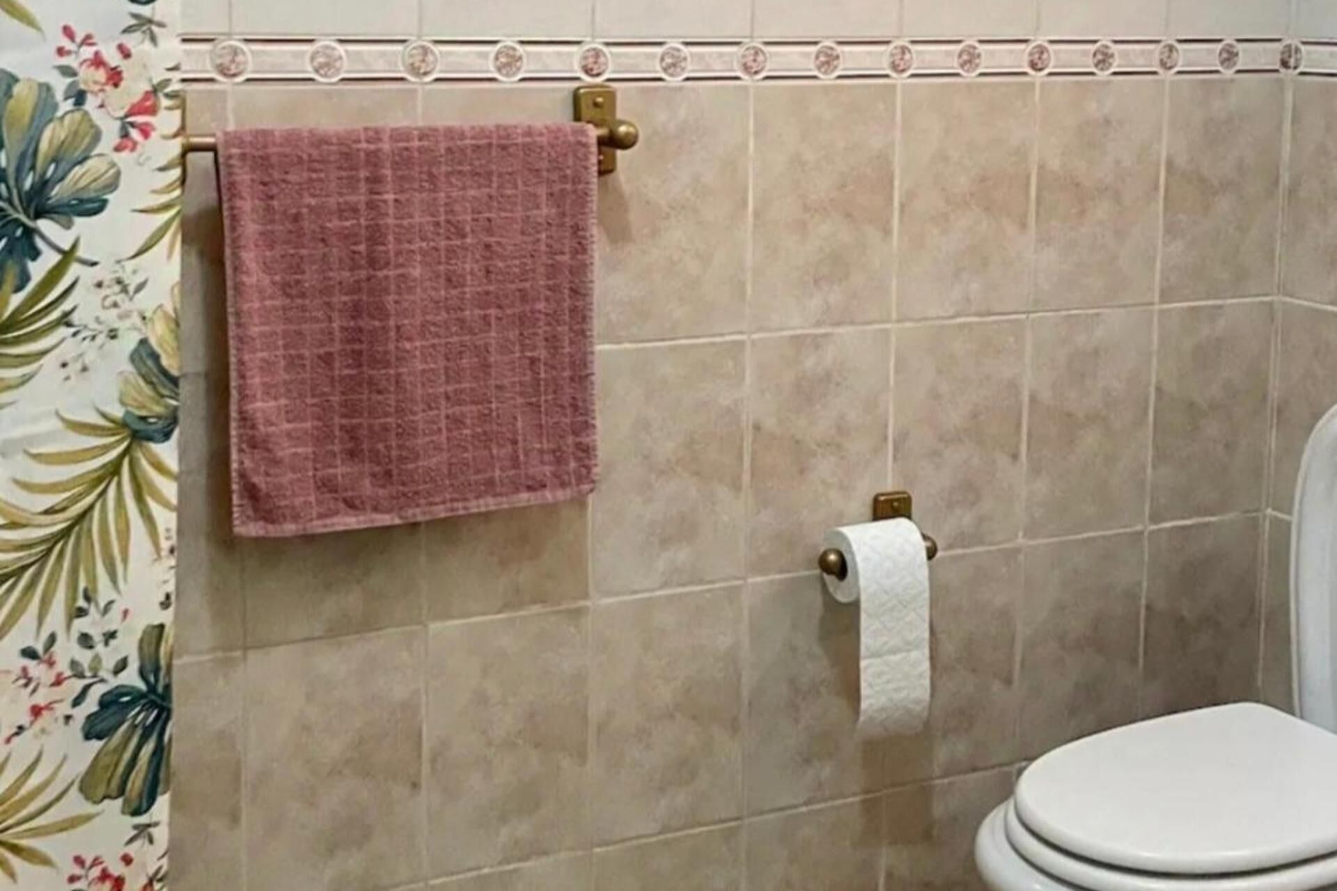 Une salle de bain avec des toilettes, une serviette rose suspendue à un porte-serviettes et un support à papier toilette.