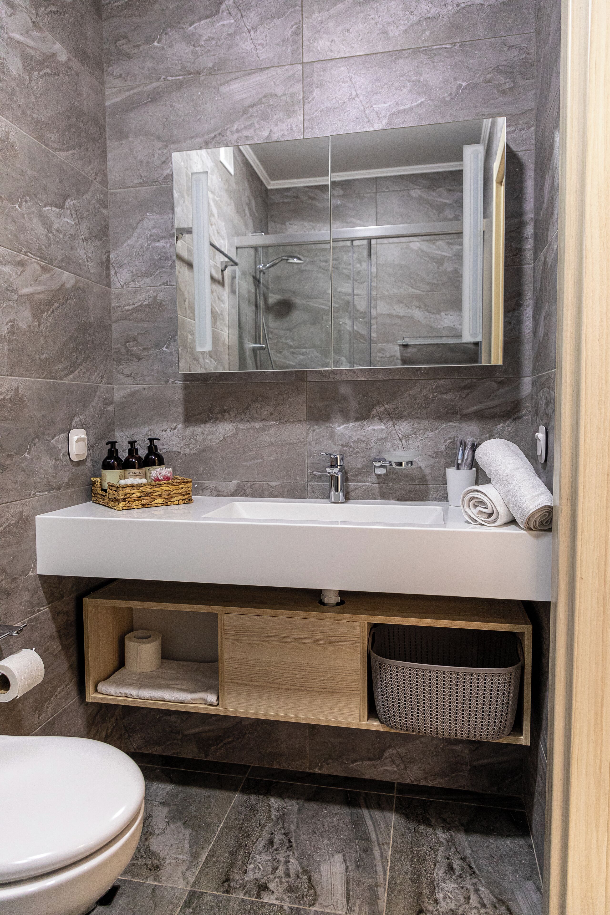 A modern bathroom with a marble wall, a white sink, a mirror, and a toilet.