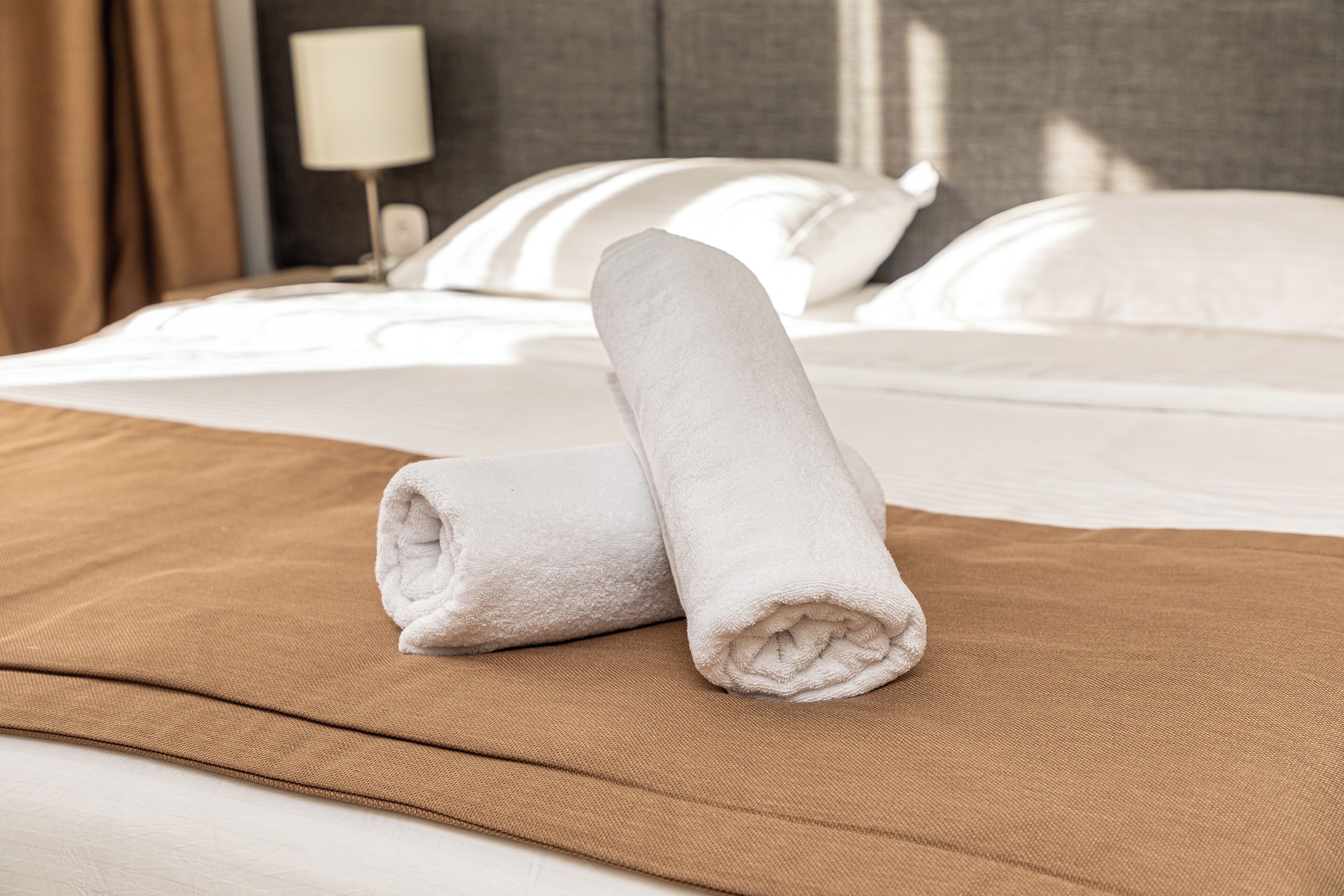 Una cama bien hecha con una colcha marrón y dos toallas blancas enrolladas sobre ella.