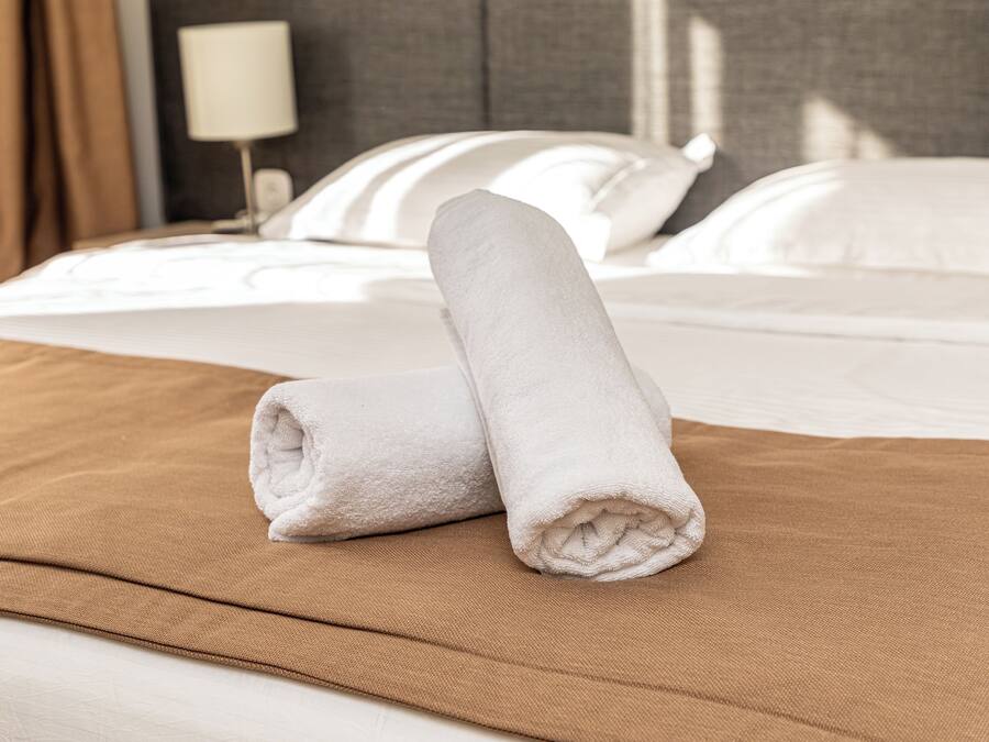 Una cama bien hecha con una colcha marrón y dos toallas blancas enrolladas sobre ella.