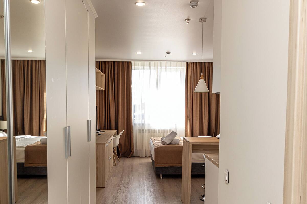 A hotel room with a wooden floor, a bed, a desk, and a wardrobe.