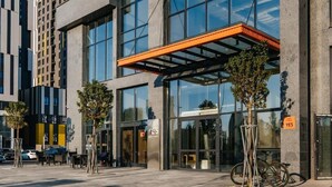 Een modern gebouw met grote ramen en een glazen ingang. Buiten staan bomen en is een fiets geparkeerd.