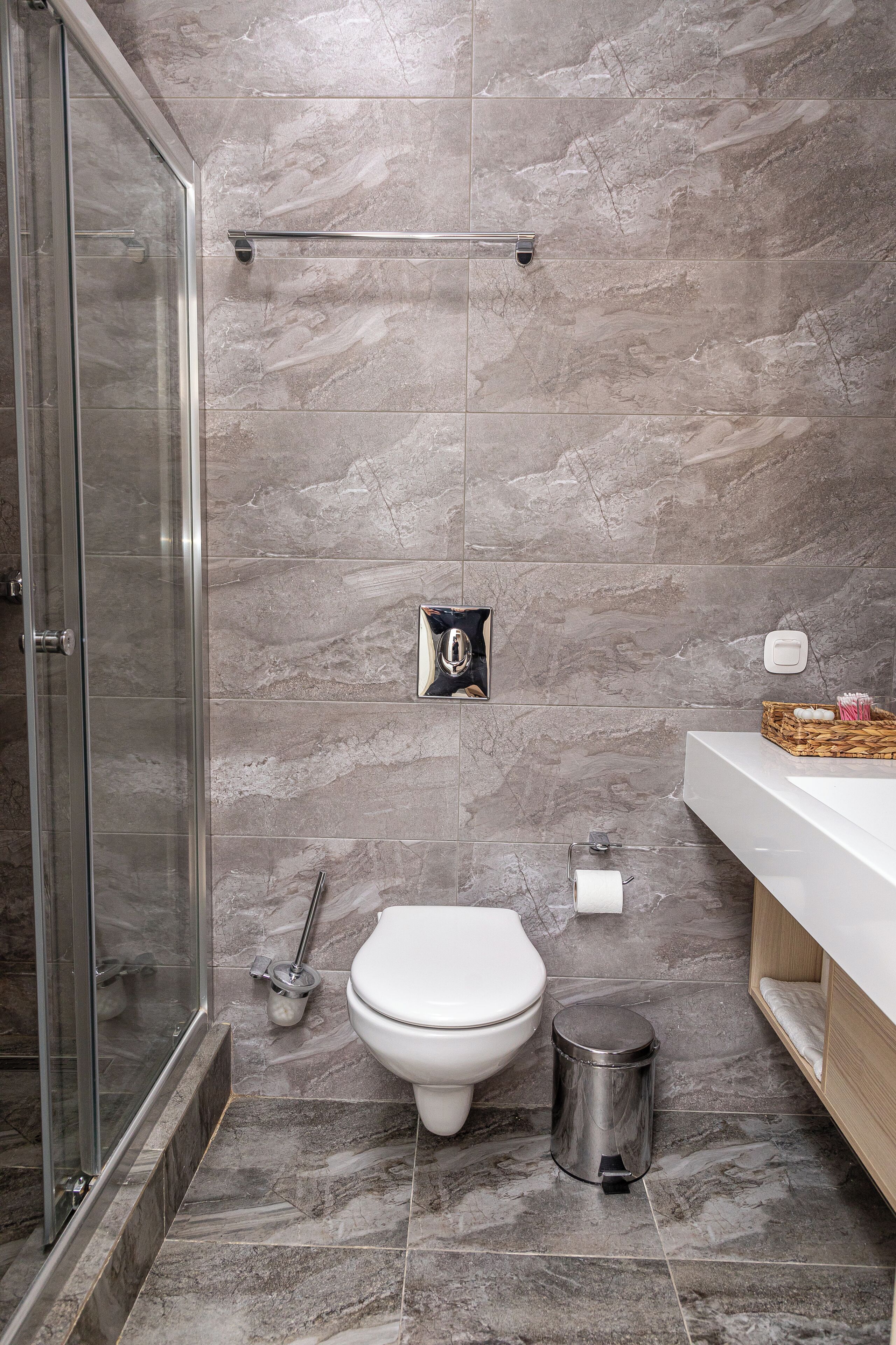 Un baño moderno con cabina de ducha de vidrio, inodoro, cubo de basura y tocador con espejo.