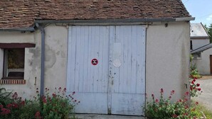 A building with a tiled roof and a white door. There is a red sign on the door and flowers in front.