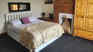 A bedroom with a bed, a wooden wardrobe, a brick wall, and a framed picture on the wall. - Cottage - Sleeps 4 - Garden - Parking (Chorley)