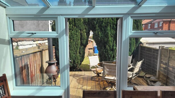 A conservatory with a view of a backyard patio area, including a table and chairs, a wooden fence, and a chimney. - Cottage - Sleeps 4 - Garden - Parking (Chorley)