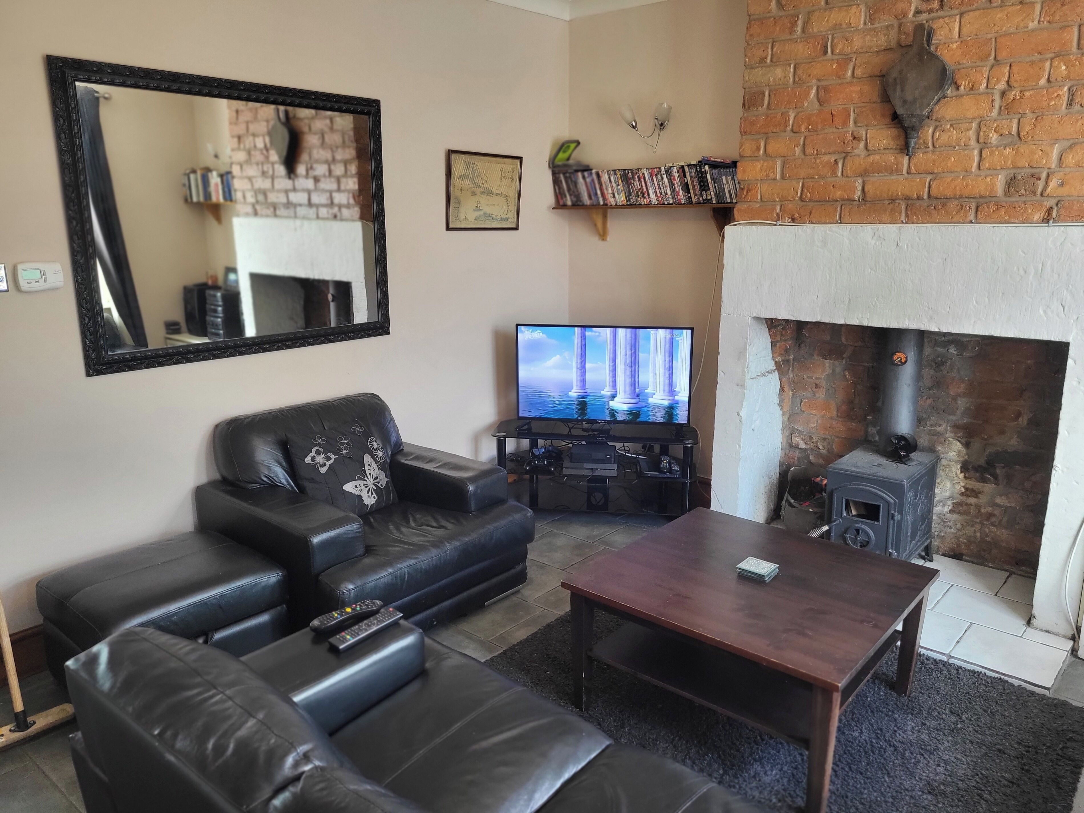 A living room with a black leather sofa, a wooden coffee table, a TV, and a brick fireplace.