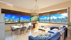 A modern living room with a large TV, a fireplace, a dining area, and a sofa with patterned cushions. - Mirsini Villa Private Pool & Jacuzzi (Georgioupoli)