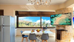 A modern kitchen with a large window, a stone fireplace, and a flat-screen TV. - Mirsini Villa Private Pool & Jacuzzi (Georgioupoli)