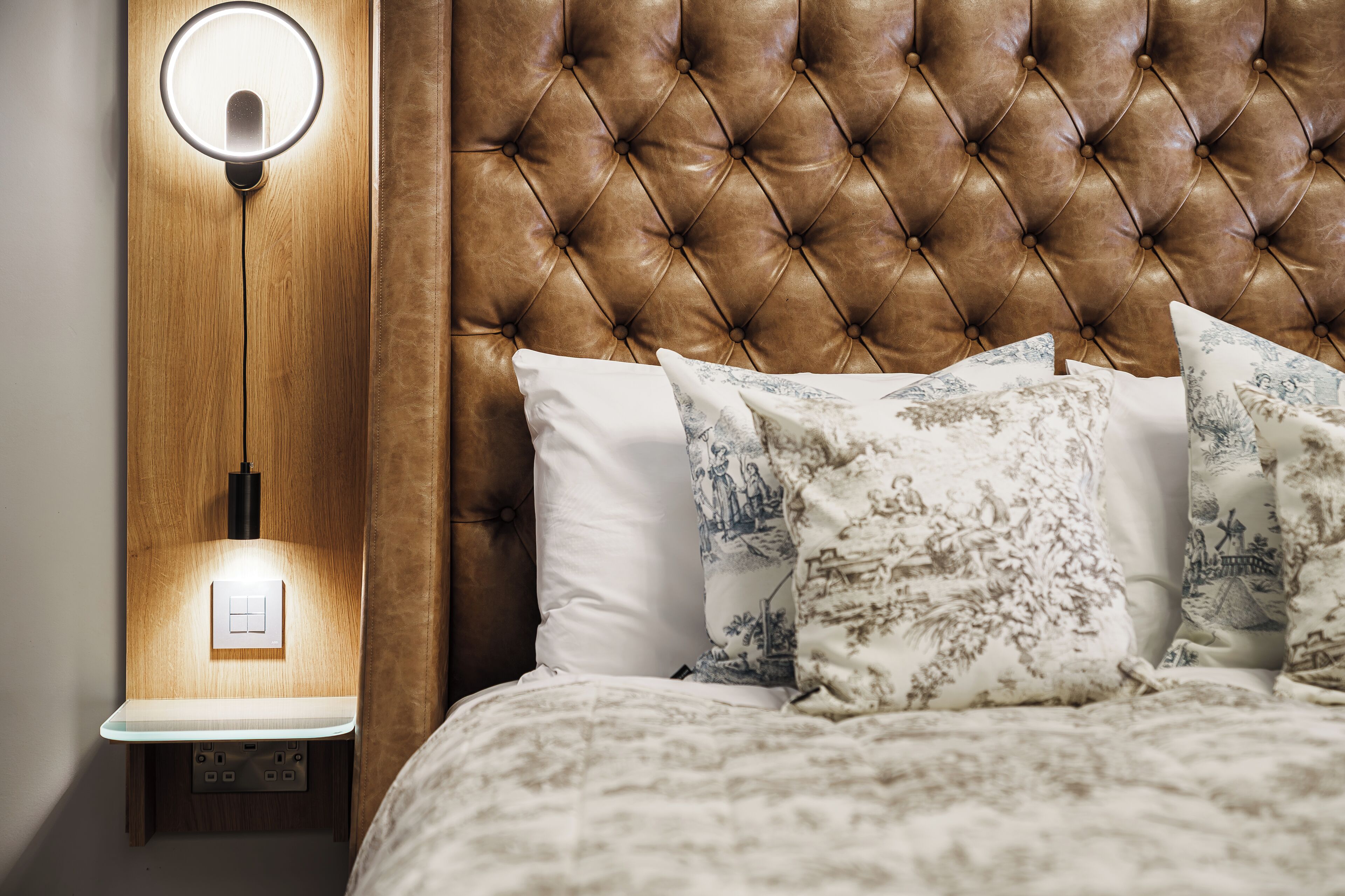 Een slaapkamer met een gebonden hoofdbord, een bedlamp en gekleurde kussens.