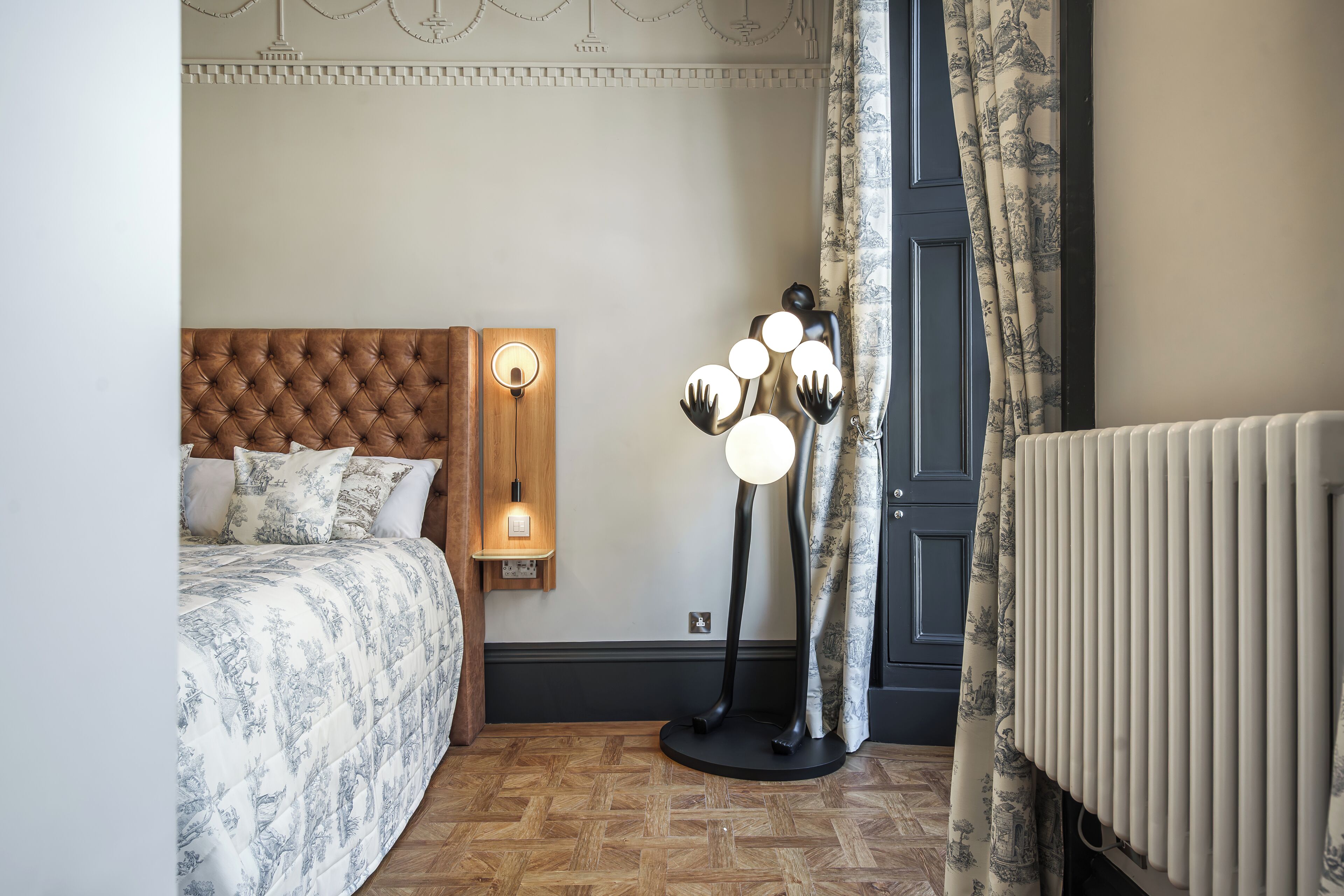 Een slaapkamer met een gestoffeerd hoofdeinde, een nachtkastje met een lamp en een radiator.