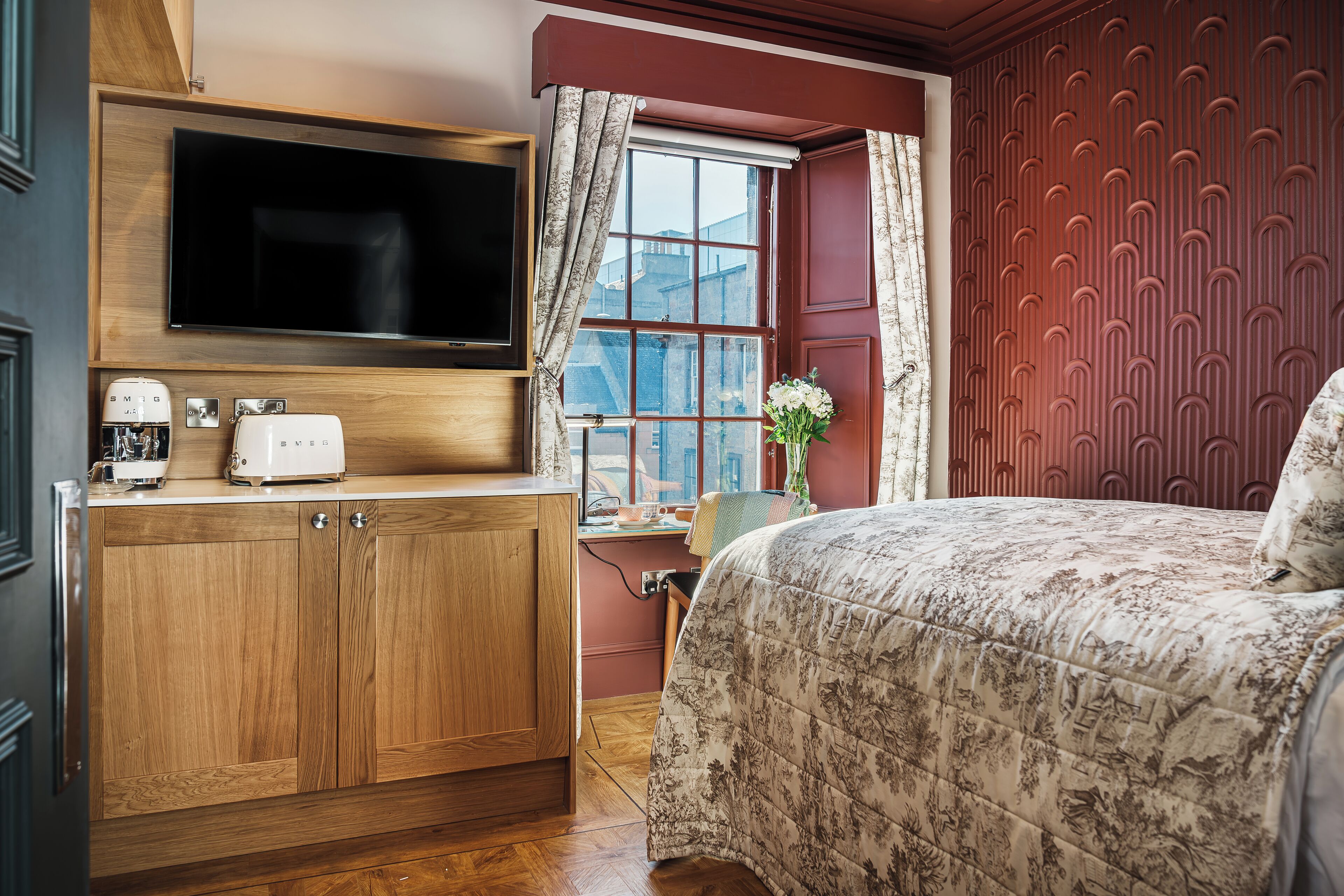 A bedroom with a bed, wooden wardrobe, built-in TV, and a window with curtains.