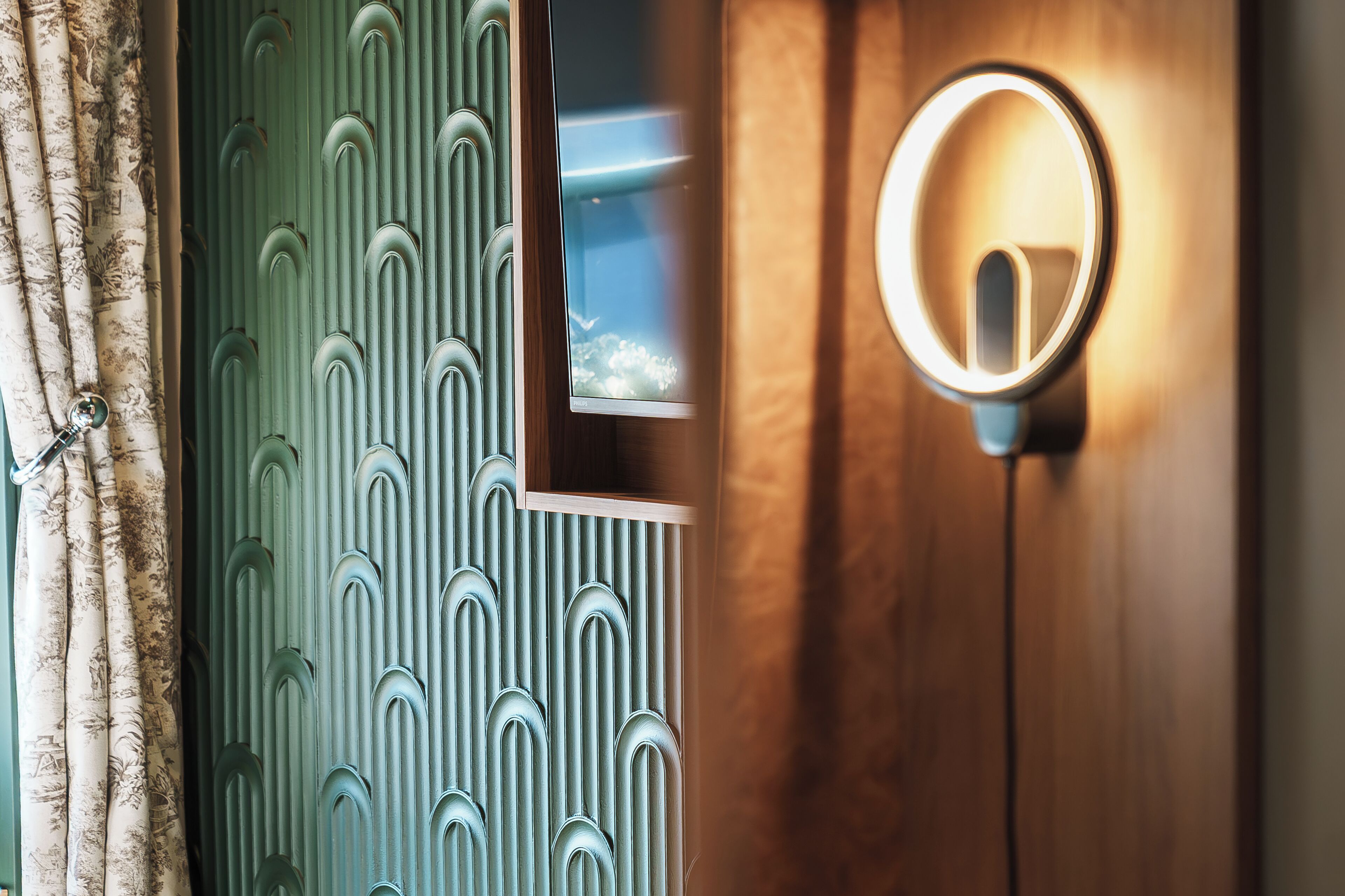 Een kamer met een houten deur, een spiegel met verlichting en een behang met patroon.