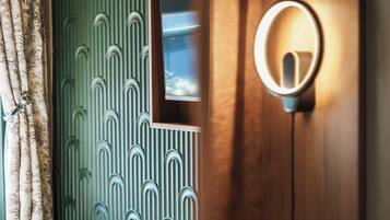 Een kamer met een houten deur, een spiegel met verlichting en een behang met patroon.