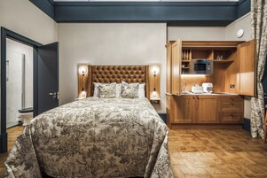A bedroom with a large bed, a wooden headboard, bedside lamps, and a built-in wooden cabinet with a microwave.