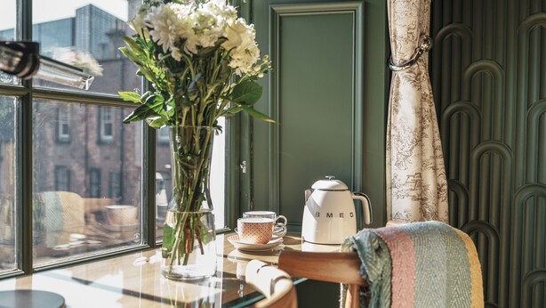 A table with a vase of flowers, a cup, and a coffee maker. - Bonnie Hotel - Smart Boutique ApartHotel - Haymarket Edinburgh (Edinburgh)