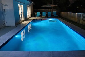 Ein Schwimmbecken mit einer gefliesten Liegefläche, Liegestühlen und einem Zaun.