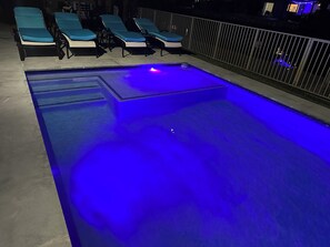 Une piscine éclairée de lumières bleues, entourée de chaises longues et d’une clôture.