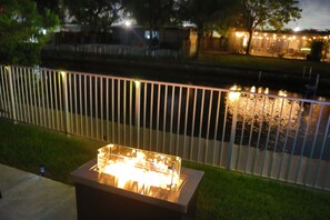 Una parrilla iluminada en el exterior, con una valla de metal y un cuerpo de agua al fondo.